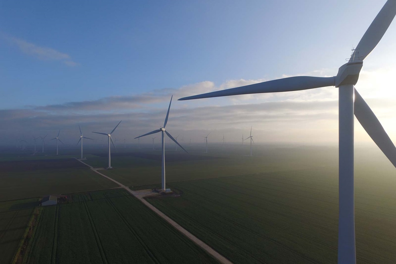 Aerial view of a wind farm with multiple turbines against a blue sky and fields, showcasing renewable energy.