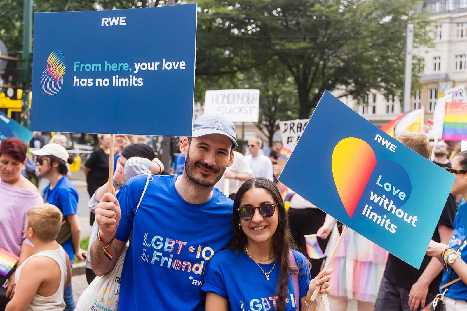 Teilnehmer halten bunte Schilder bei einer Parade. Auf einem Schild steht: 'Von hier hat deine Liebe keine Grenzen'.