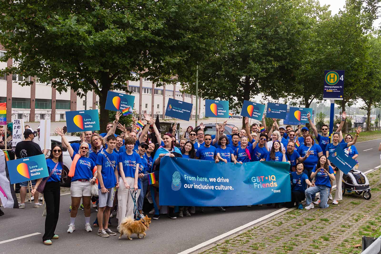 Teilnehmer halten bunte Schilder bei einer Parade. Auf einem Schild steht: 'Von hier hat deine Liebe keine Grenzen'.