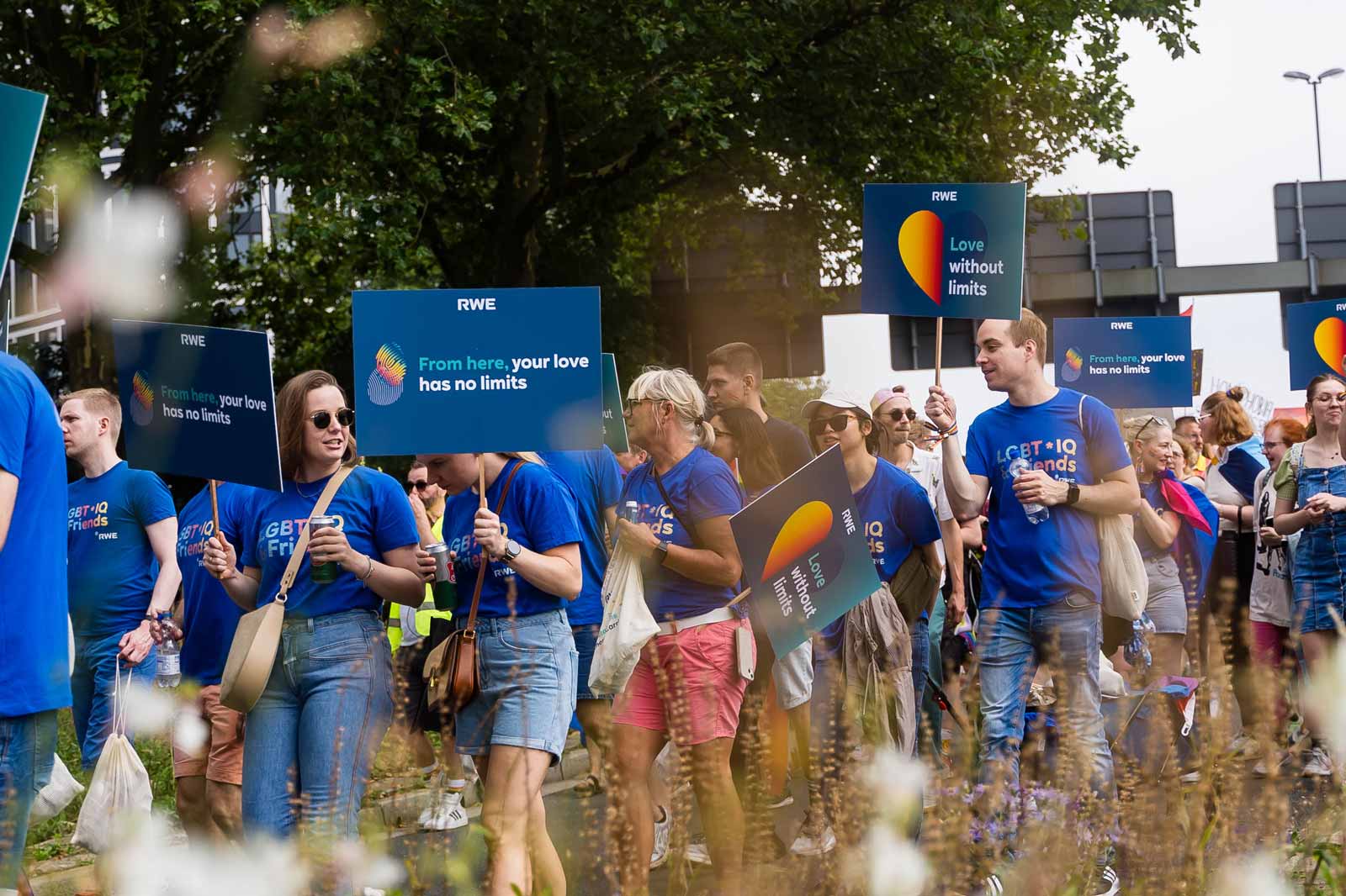 Teilnehmer halten bunte Schilder bei einer Parade. Auf einem Schild steht: 'Von hier hat deine Liebe keine Grenzen'.