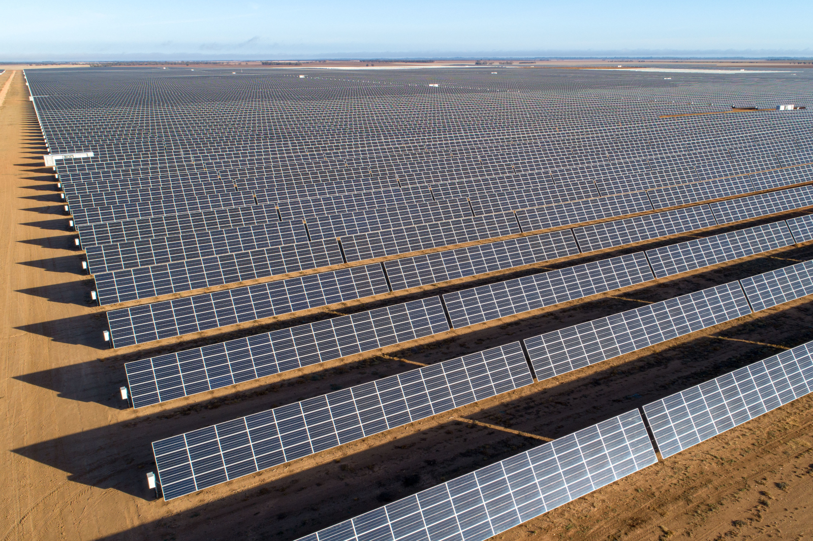 Ein weites Sonnenfeld mit mehreren Reihen von Solarpanels, die in der Sonne glänzen, erstreckt sich bis zum Horizont.