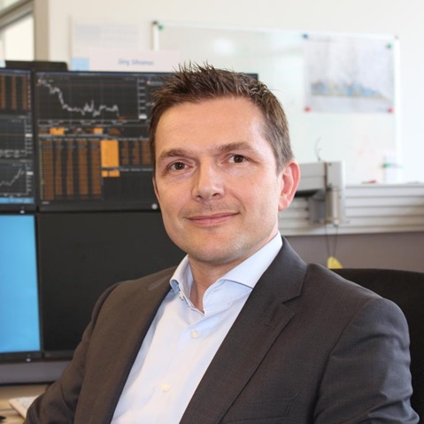 Ein Mann in einem Anzug sitzt vor mehreren Computerbildschirmen mit Finanzdaten und Diagrammen. Portrait von Jörg Silvanus.