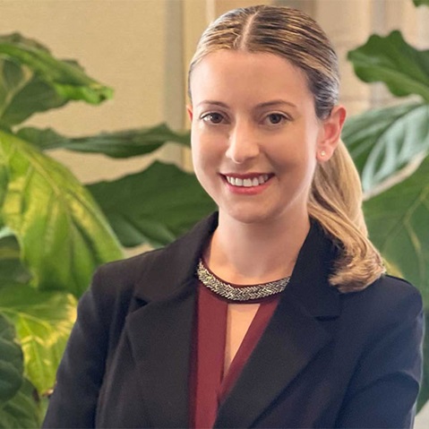 Eine Person in einem schwarzen Blazer posiert vor grünen Pflanzen.