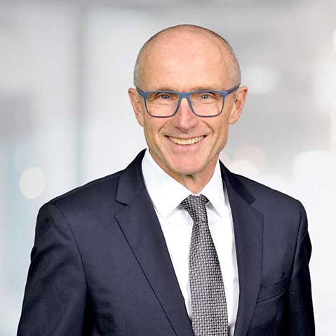 Ein Mann in einem formellen Anzug und einer Krawatte steht vor einem sanft verschwommenen Hintergrund, Portrait von Madlen Krembel.