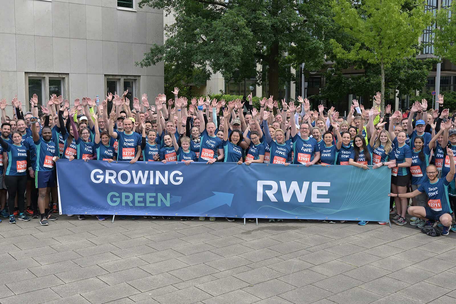 Eine Gruppe von Laufenden hebt die Hände vor einem Banner mit der Aufschrift 'GROWING GREEN' und 'RWE'.