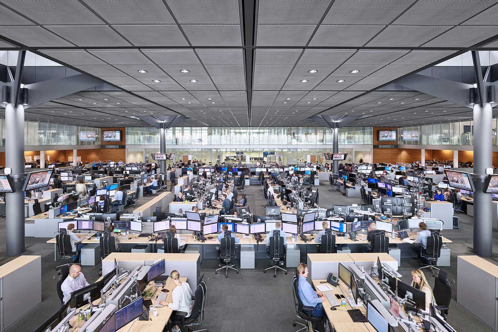 Eine moderne Büroumgebung mit zahlreichen Arbeitsplätzen und Computermonitoren, die von Mitarbeitern genutzt werden.