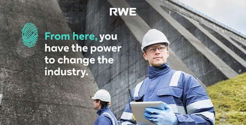A worker in blue overalls and a helmet holds a tablet in front of a dam. The surroundings are green and industrial.