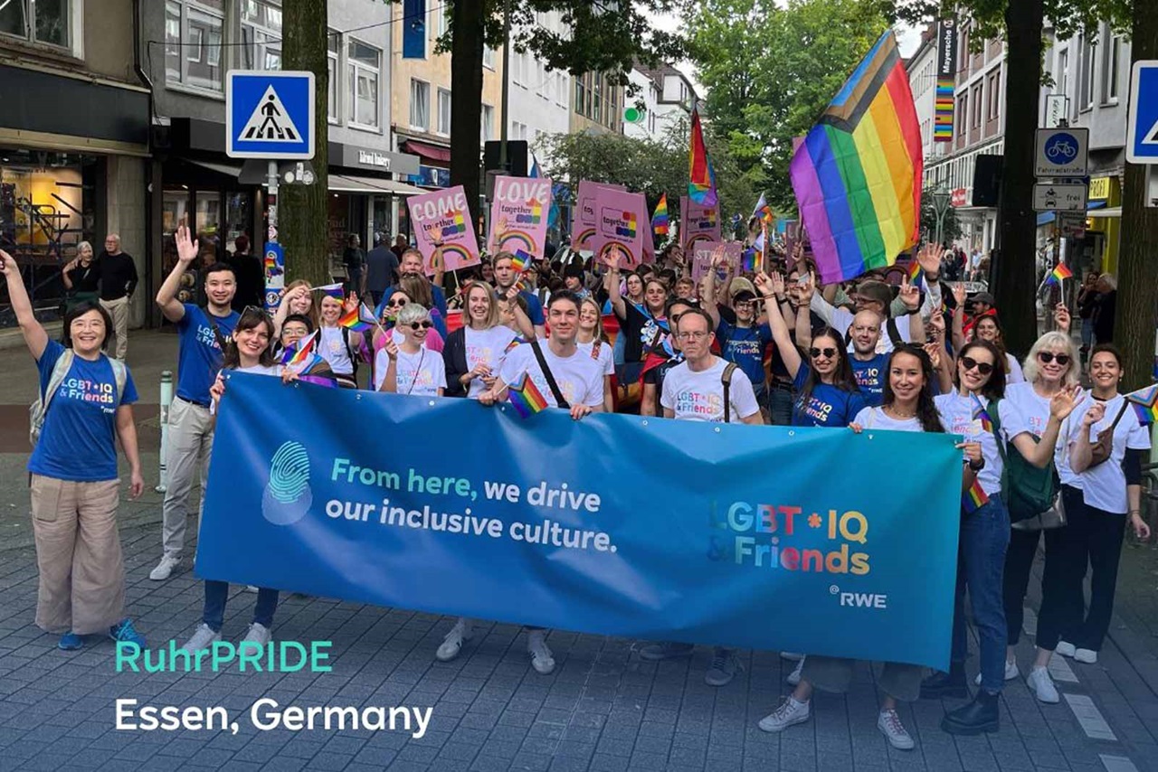 A group of people with rainbow flags celebrates at RuhrPride in Essen, Germany, while holding a banner.