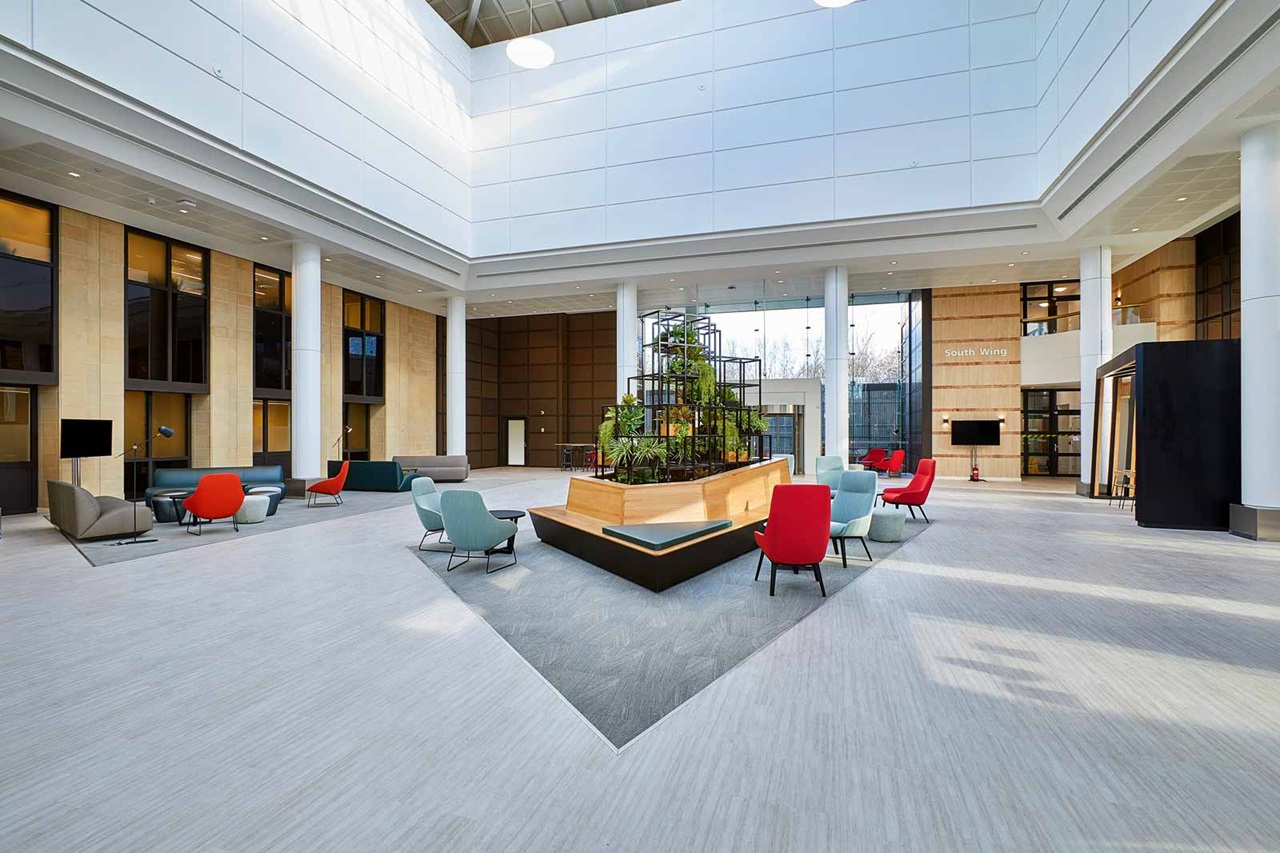 A bright indoor space featuring modern seating areas and a central plant installation. Large windows enhance natural light.