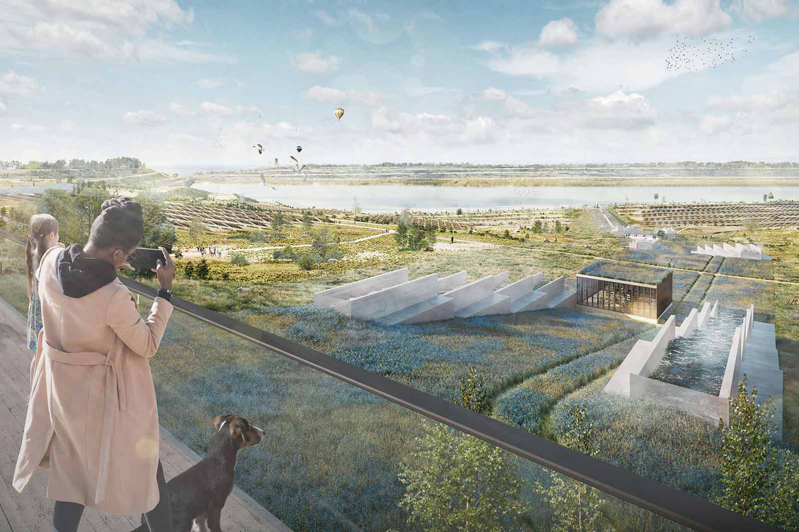 Eine Frau macht ein Foto von einer malerischen Landschaft mit einem Fluss, moderner Architektur und Grünflächen im Vordergrund.