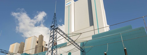 A blue and white industrial building complex with power lines and clouds in the sky.