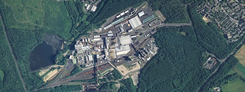 Aerial view of an industrial site surrounded by forest and a small pond.
