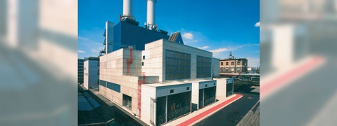 A modern industrial building featuring two tall chimneys and a grey façade under a clear blue sky.