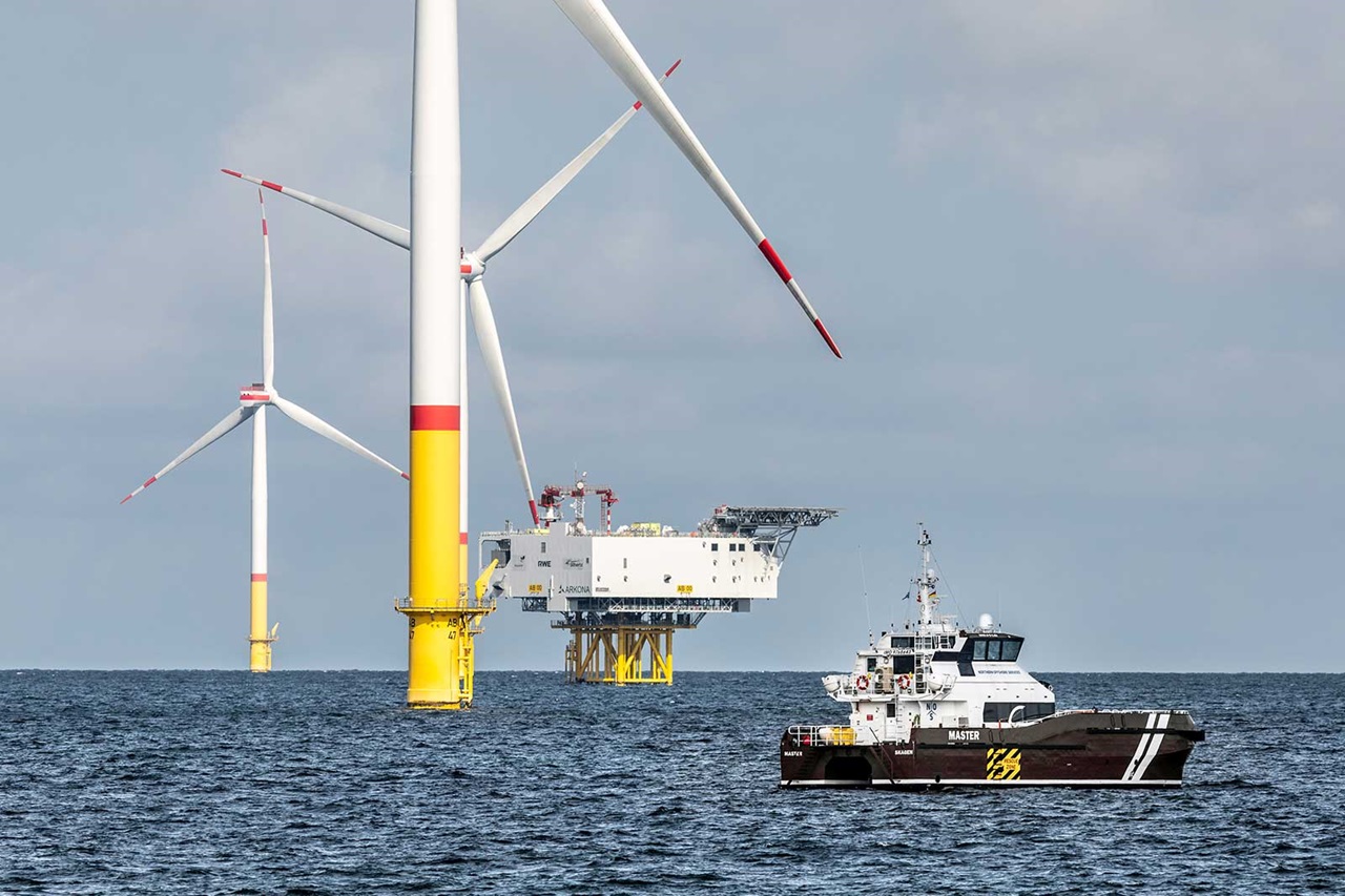 Offshore wind turbines with a boat in the foreground on open water under a cloudy sky.