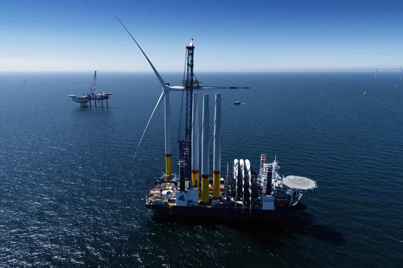 A large offshore wind turbine installation vessel with multiple turbines and a drilling platform in the background.