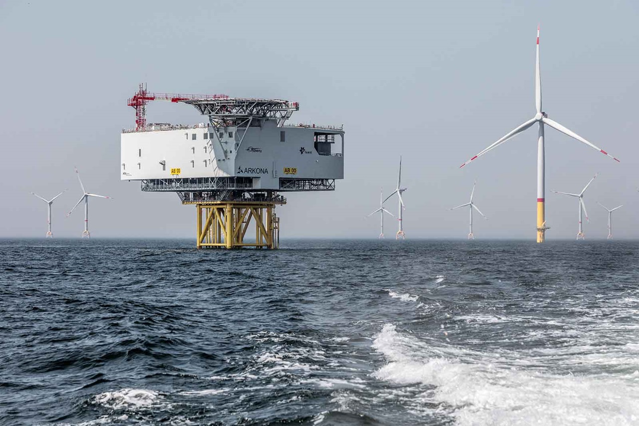 An offshore wind farm featuring a large substation and several wind turbines in the background amidst calm water.