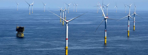 A series of wind turbines in the sea against a blue sky. A platform stands in the foreground.