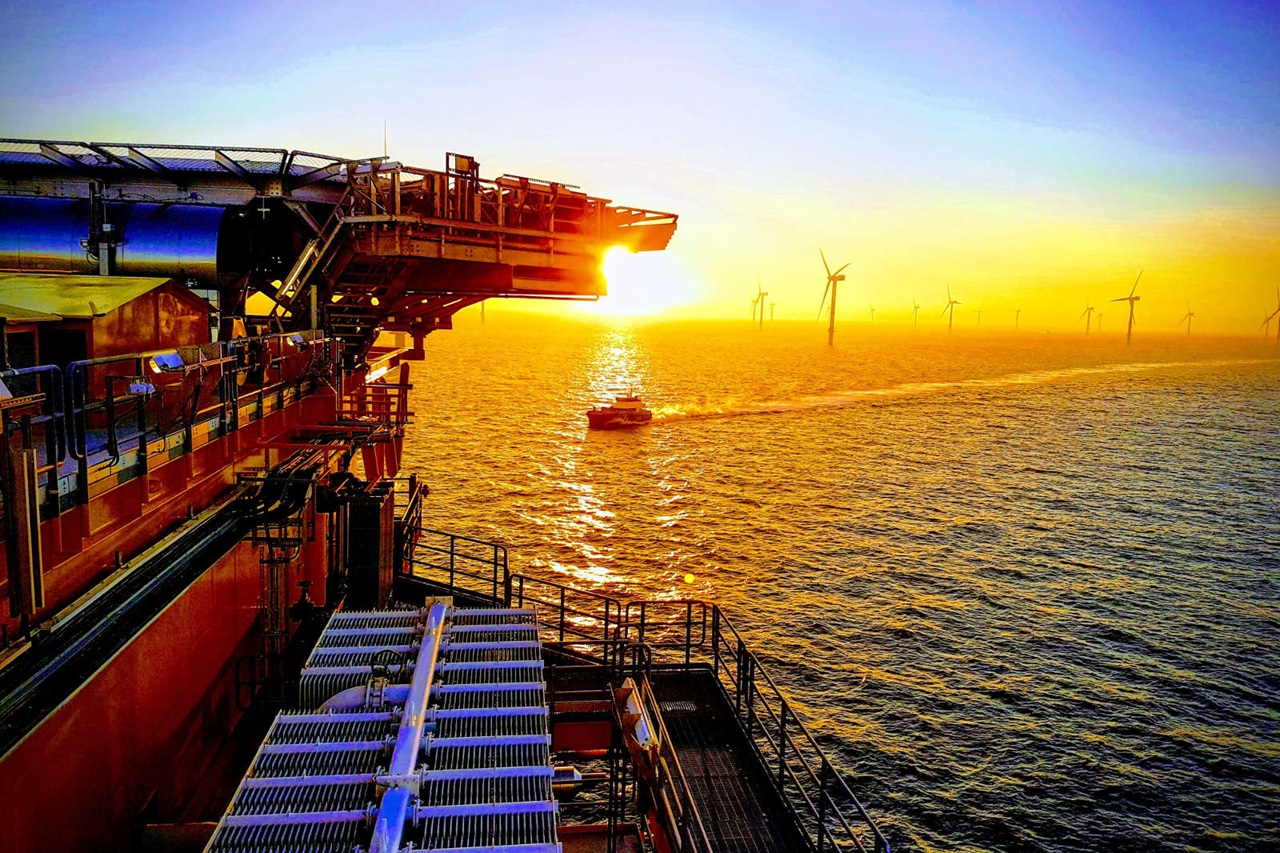 A sunset over the sea, featuring a boat and wind turbines in the background.