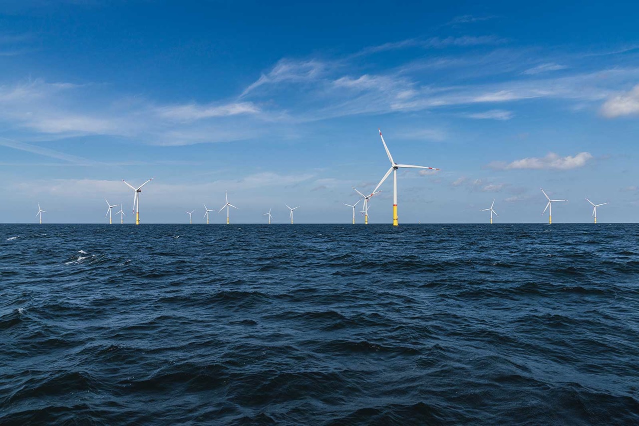 A wind farm with several turbines stands in the ocean under a clear blue sky.