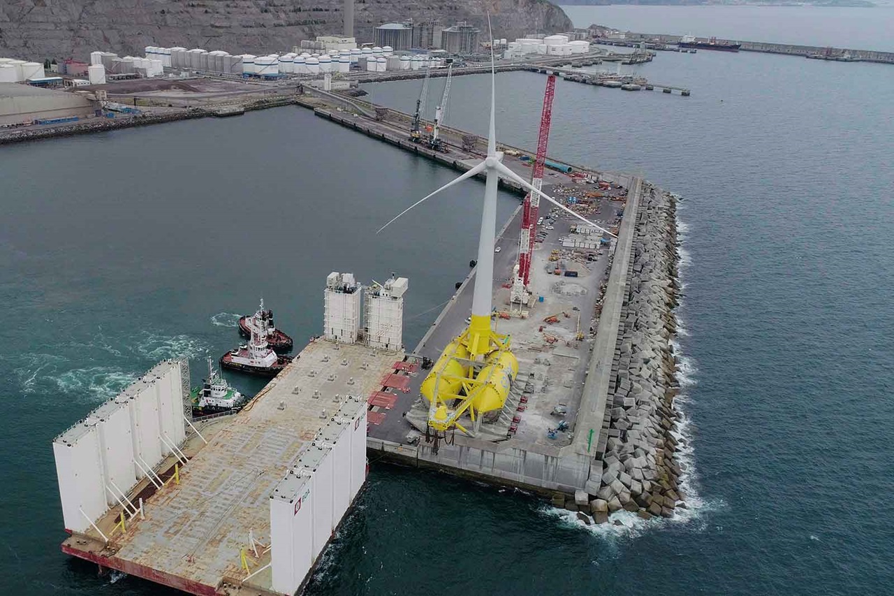 An aerial view of a harbour featuring wind turbines and vessels operating at a dock.