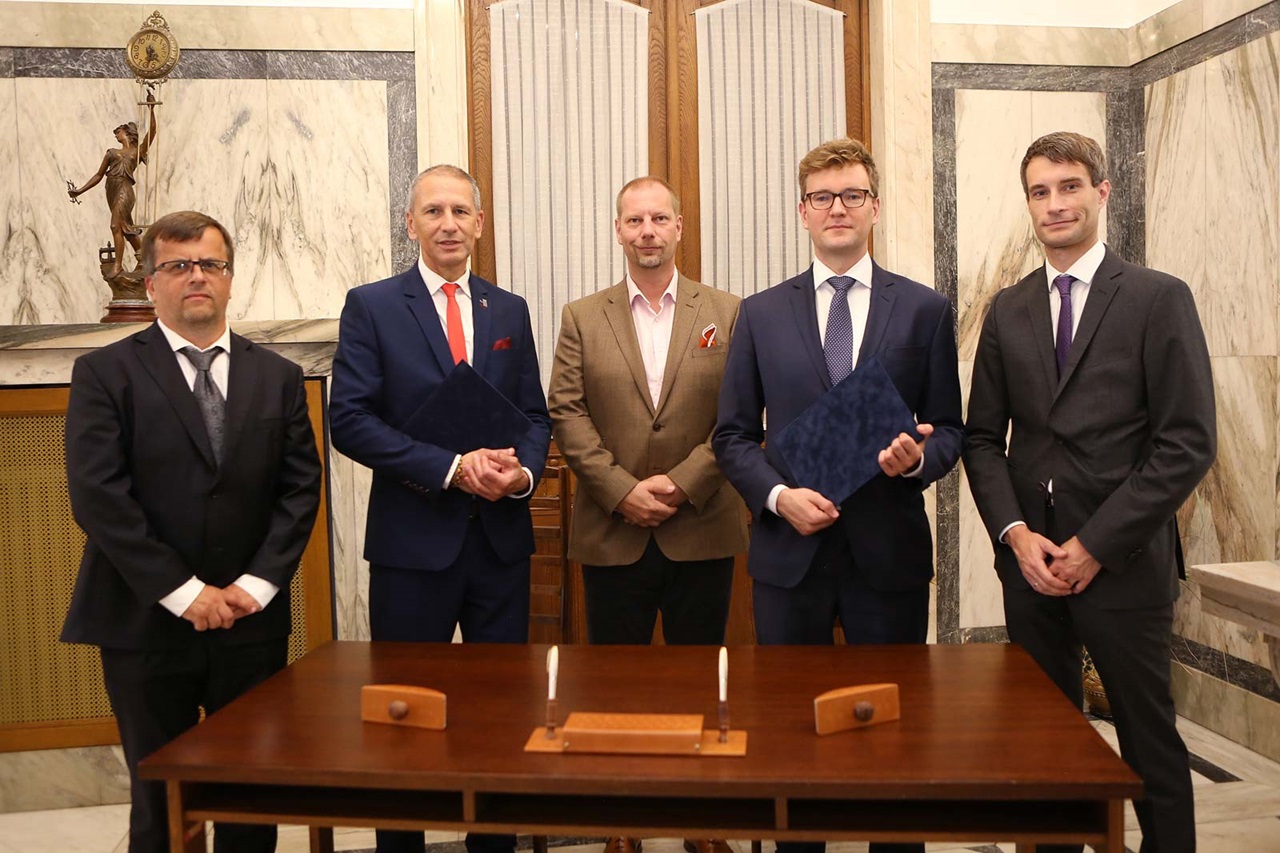 Five men in suits stand in front of a table in an elegant room with a statue and marble walls.