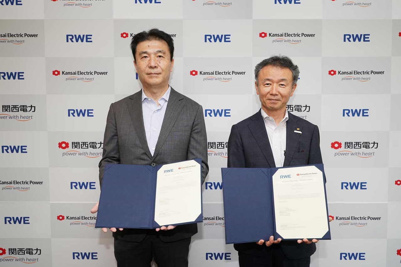 Two individuals hold documents in front of a wall featuring Kansai Electric Power and RWE logos.