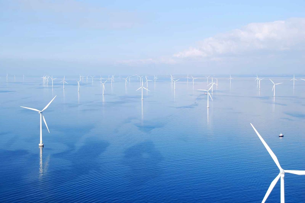 A wind turbine in the sea with multiple wind turbines in the background and calm water.