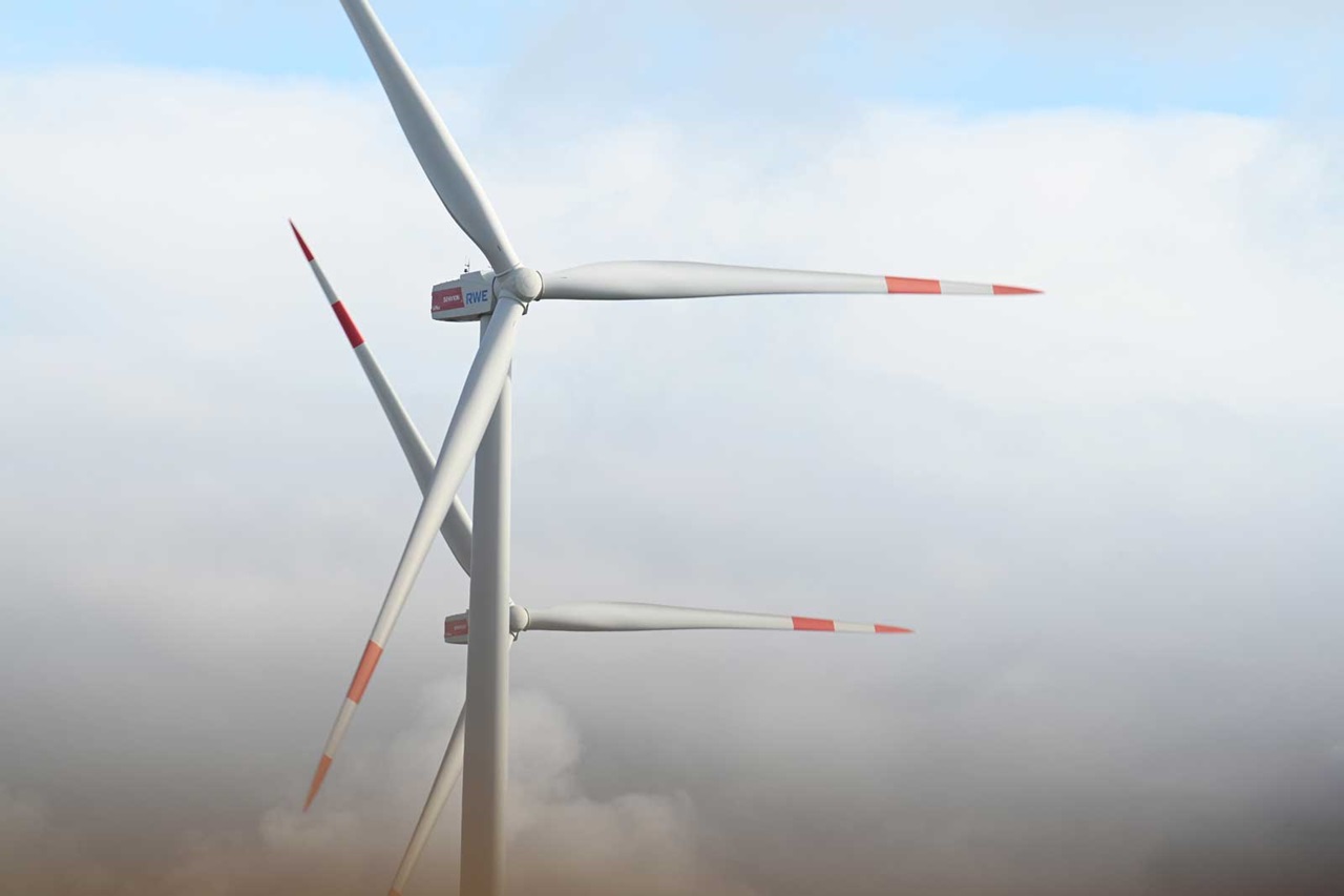 Wind turbines with white blades and red markings, partially set against a cloudy backdrop.