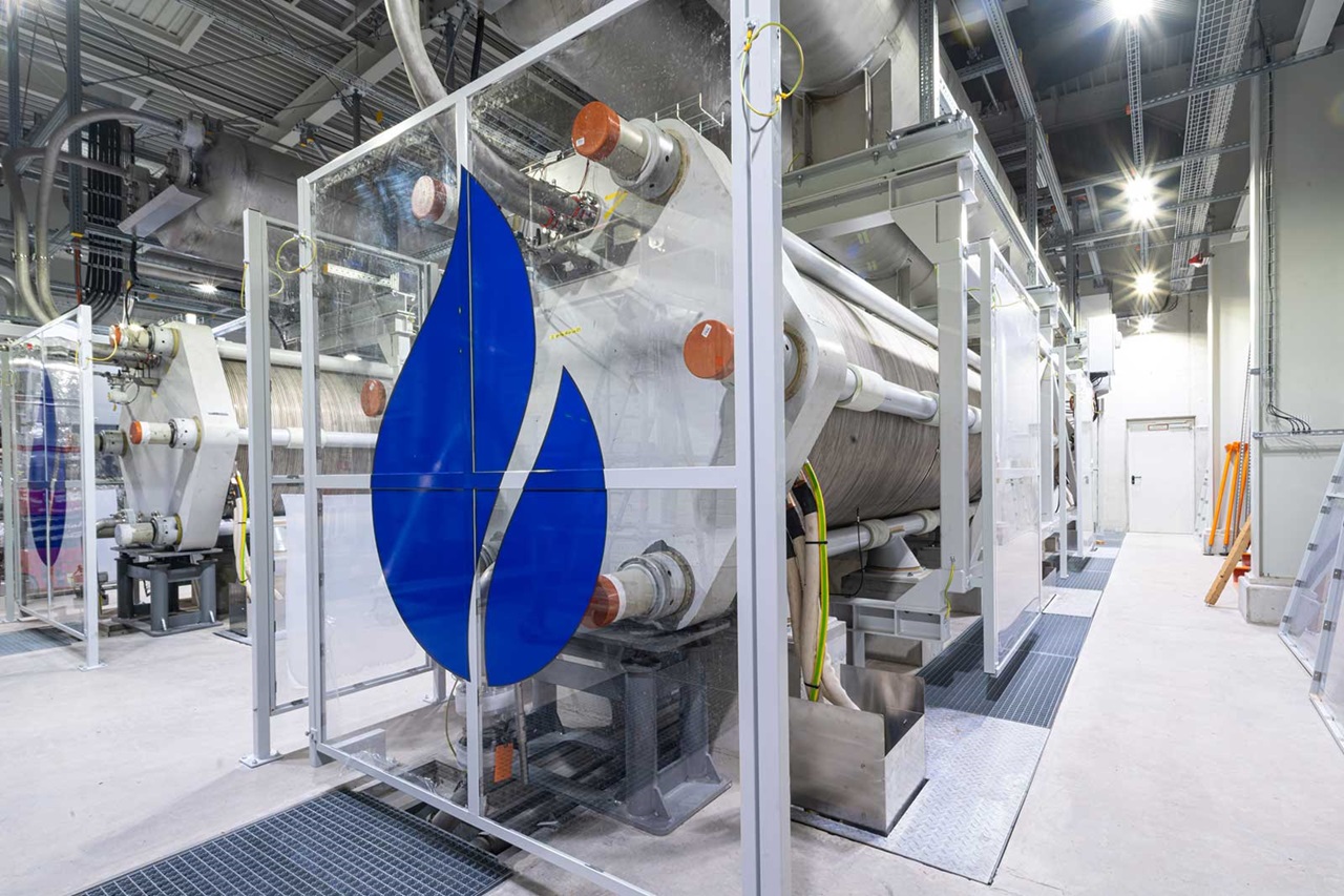 A modern industrial facility with large machines and blue water symbols on glass walls.