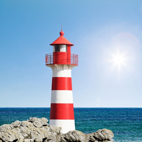 A red and white striped lighthouse stands on rocks by the sea under a clear sky.