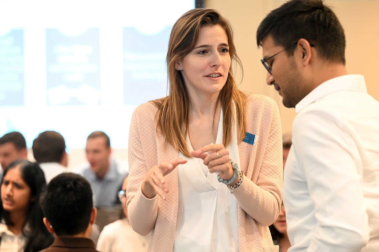 A woman is talking to a man in a conference room, while people in the background are attending an event.