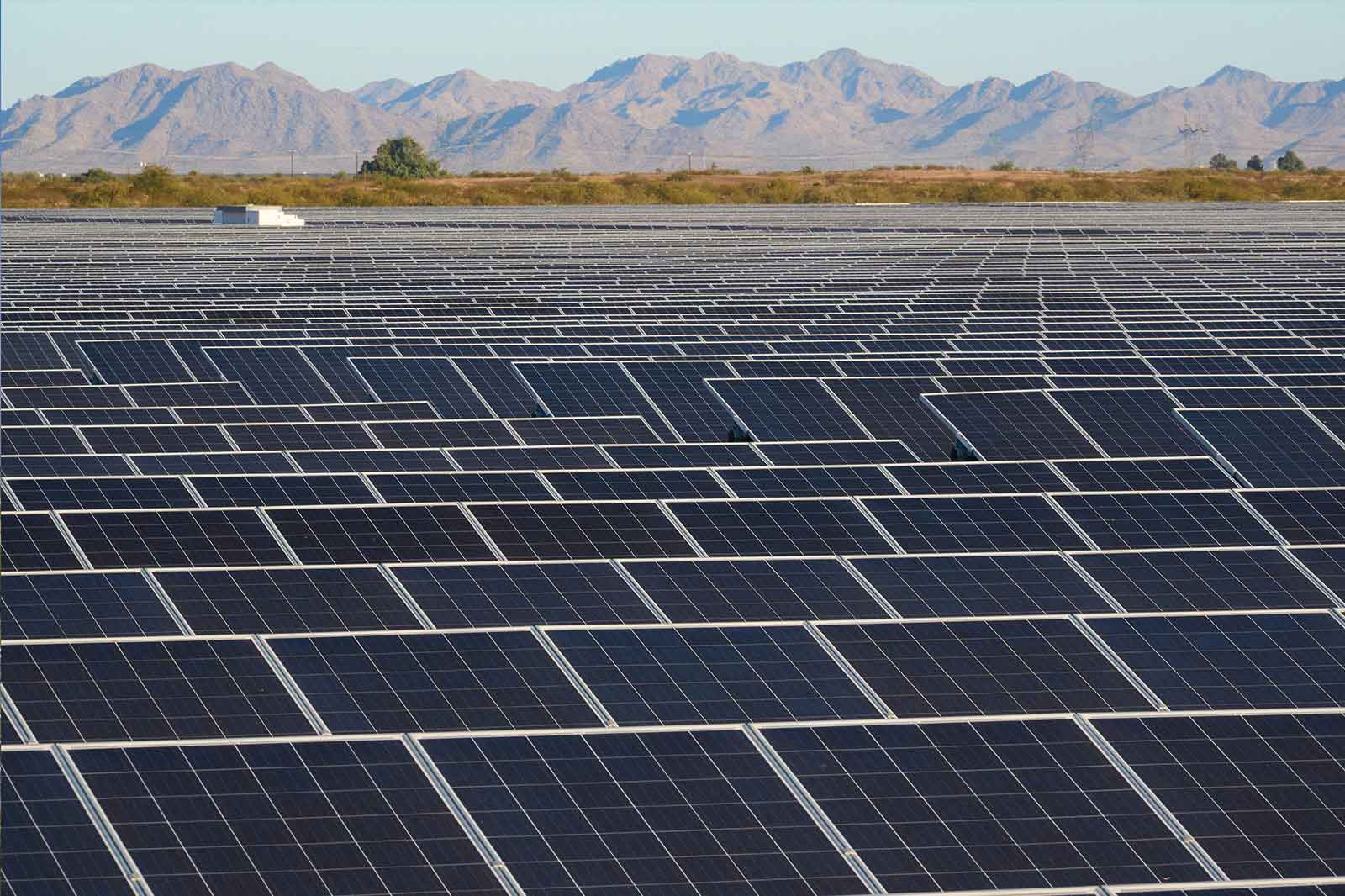 A vast solar panel field with numerous black solar panels set against a backdrop of mountains.