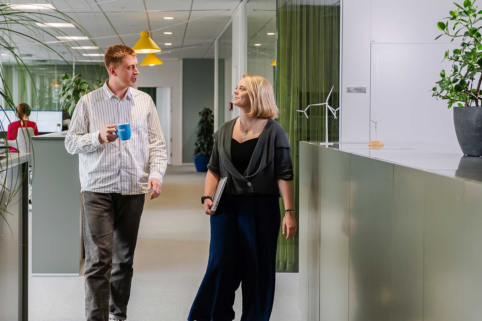 Two people walk through a modern office with plants and colourful lamps.