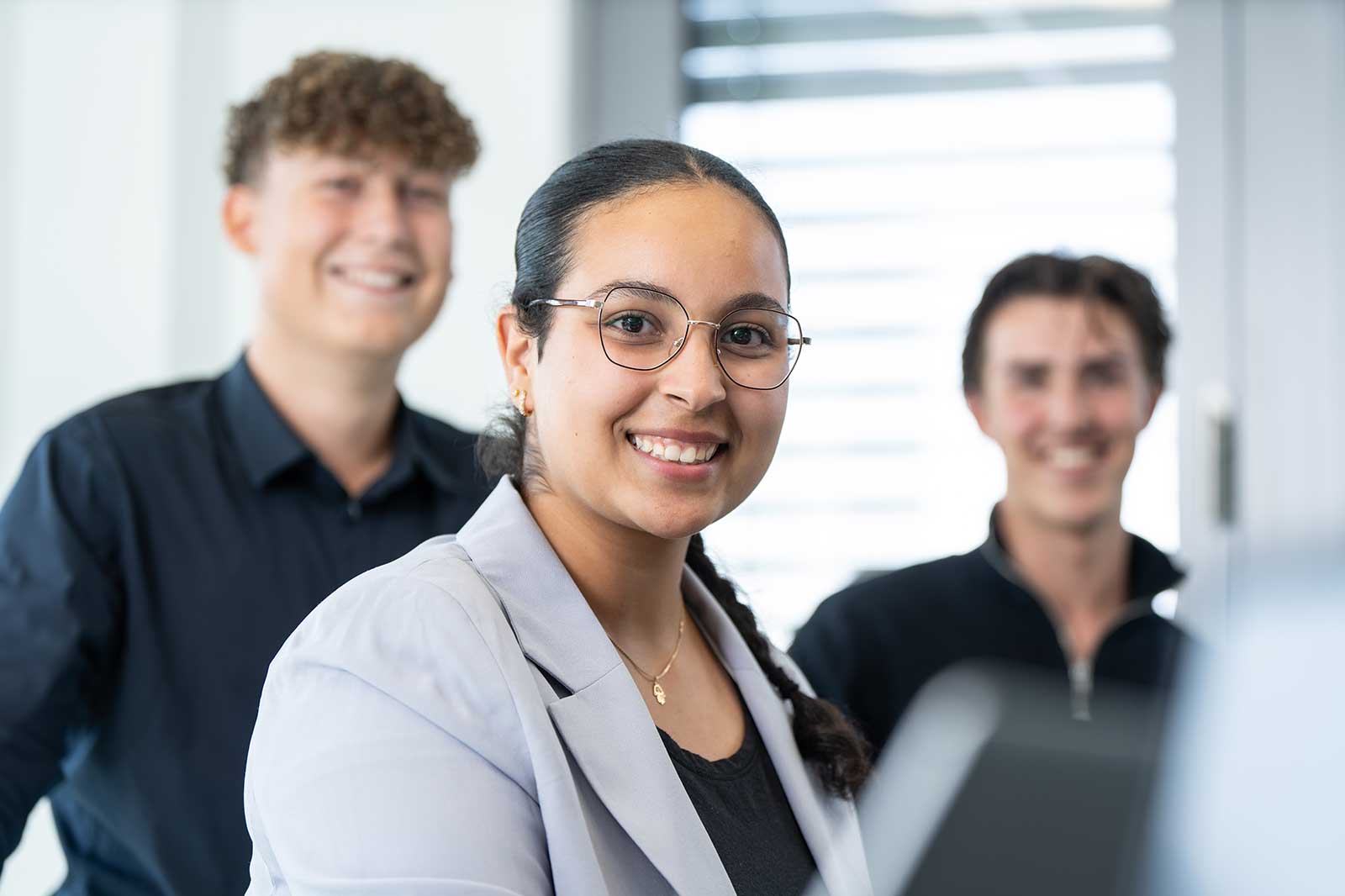 Eine Gruppe von drei Personen in einem modernen Büro, die sich auf eine Diskussion konzentrieren, mit hellem natürlichem Licht.