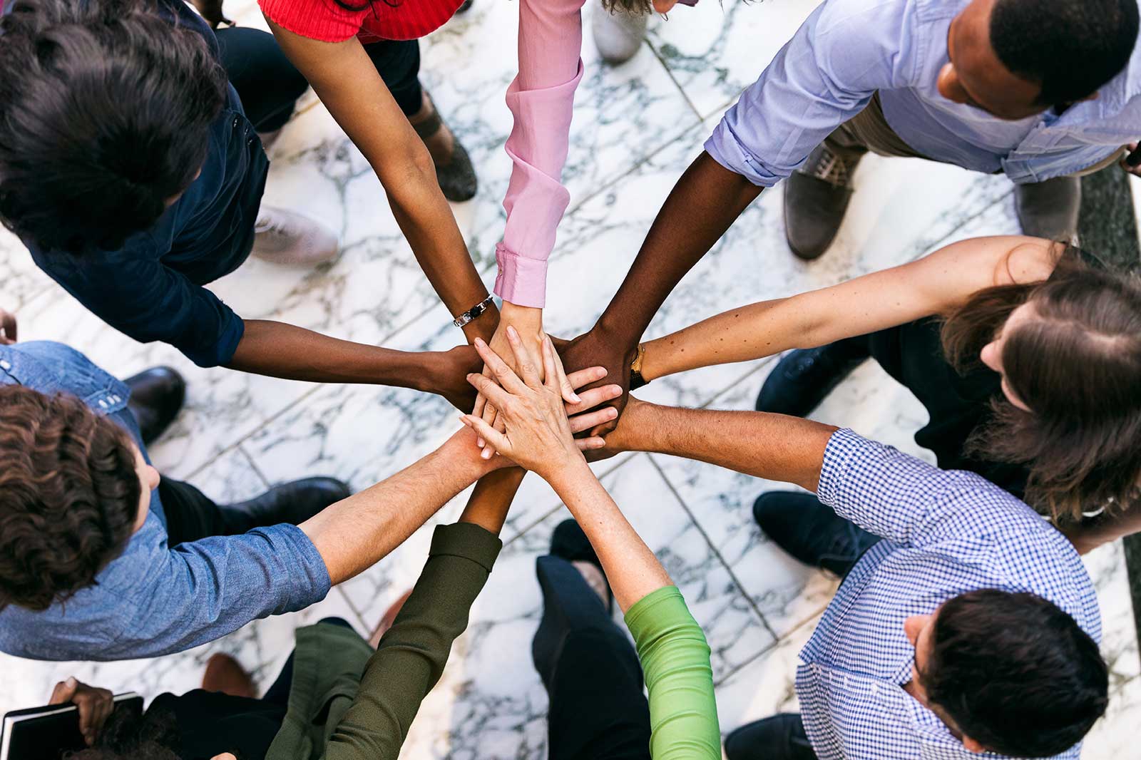 A group of people place their hands on top of each other on a marble floor, symbolising teamwork and collaboration.