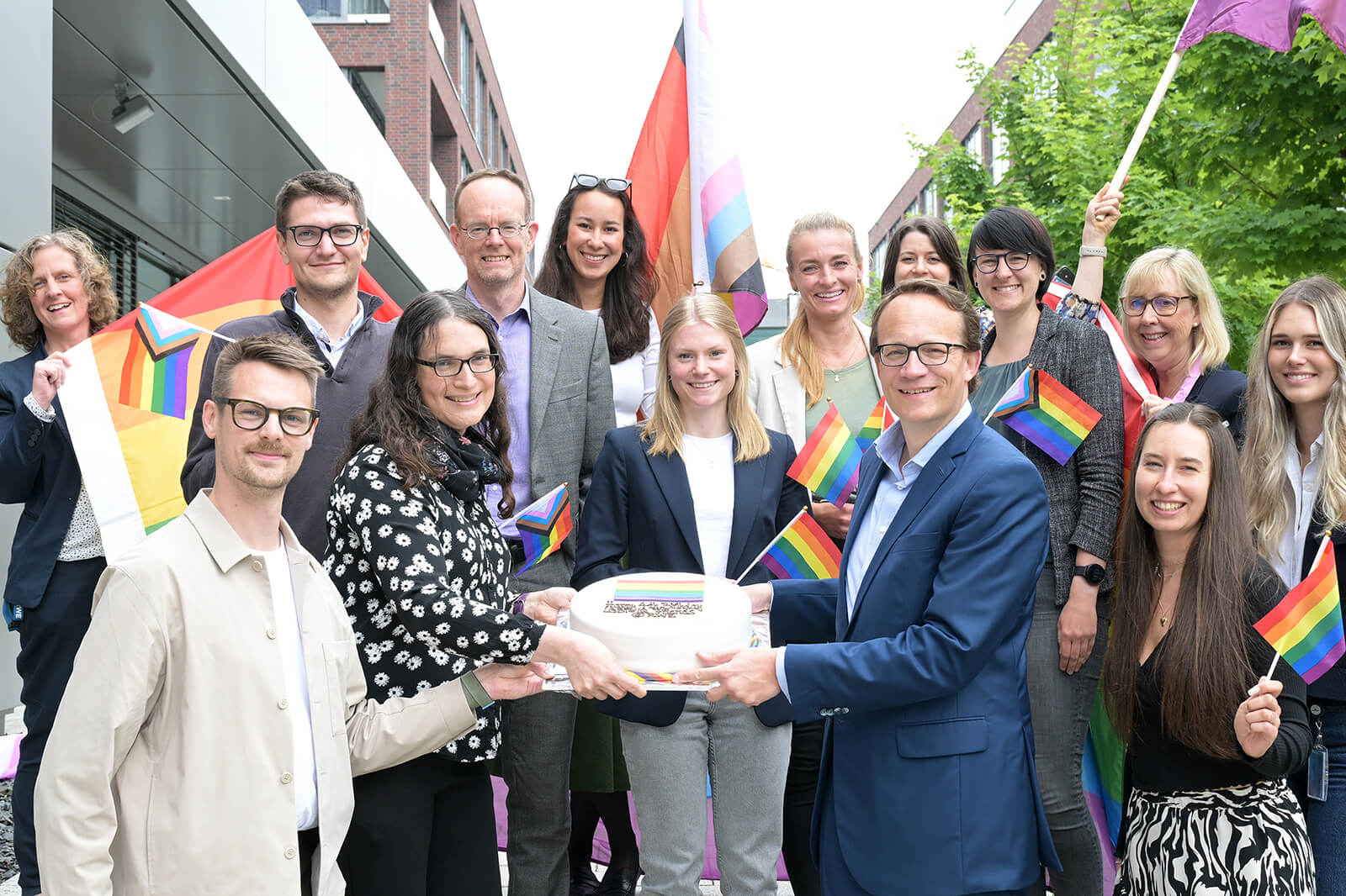 A group of people celebrating with rainbow flags and a cake, promoting inclusivity and diversity.